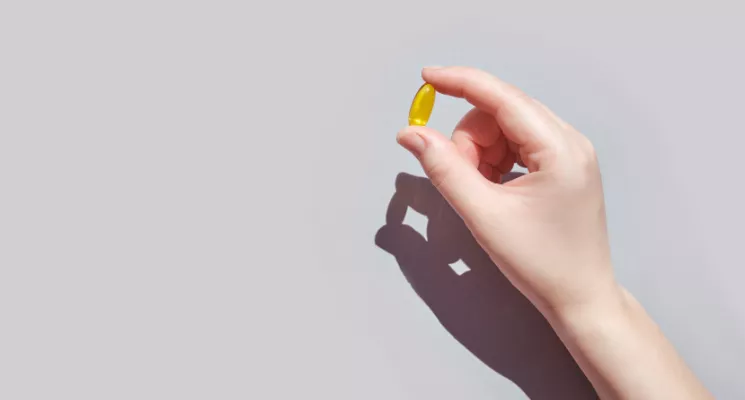 Mano sosteniendo una cápsula amarilla de complemento alimenticio